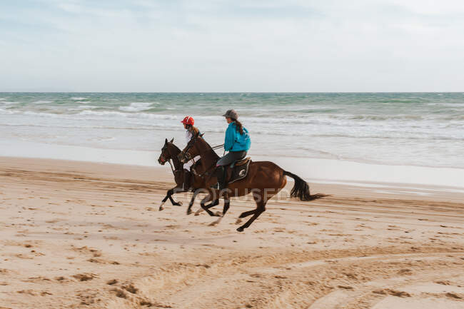 Duas mulheres montando cavalos andaluzes na praia na Espanha — Fotografia de Stock