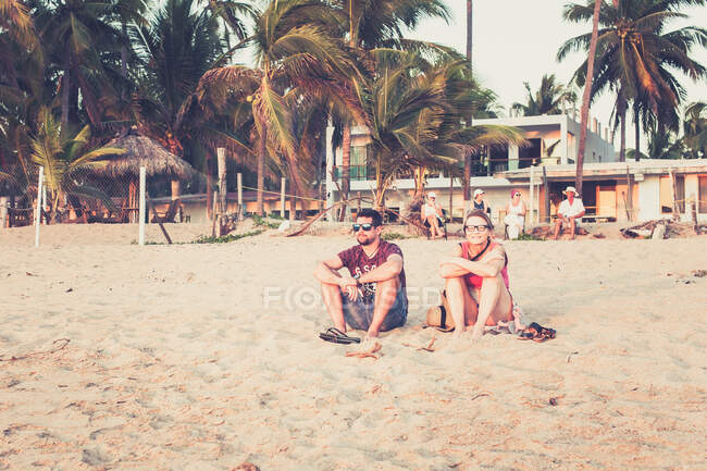 Madre e hijo sentados en la arena de México al atardecer con palmeras - foto de stock