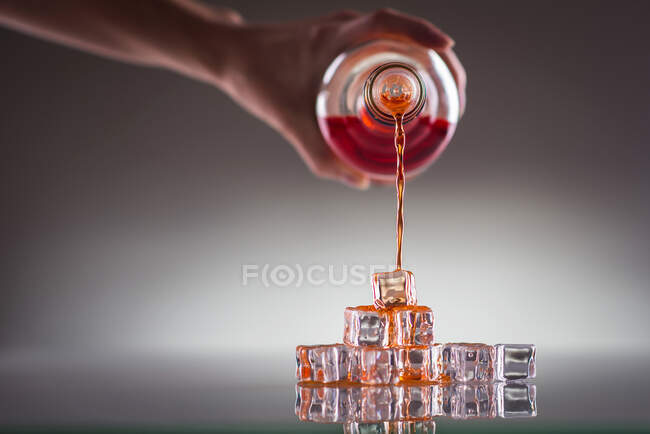 Derramando bebida vermelha sobre cubos de gelo, na superfície reflexiva — Fotografia de Stock