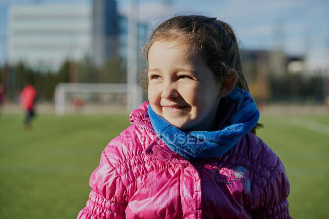 Sorrindo menina vestindo um casaco rosa em um estádio de futebol — Fotografia de Stock
