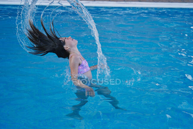 Chica en una piscina con su cabeza tirando del agua hacia atrás - foto de stock
