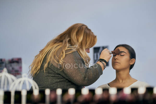 Maquillador retocando la cara y el reflejo de una modelo en el espejo - foto de stock