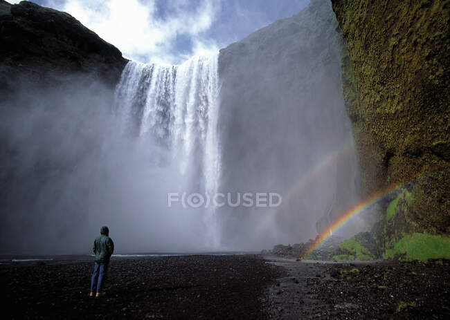 Homem de pé na frente da cachoeira Skogarfoss na Islândia — Fotografia de Stock
