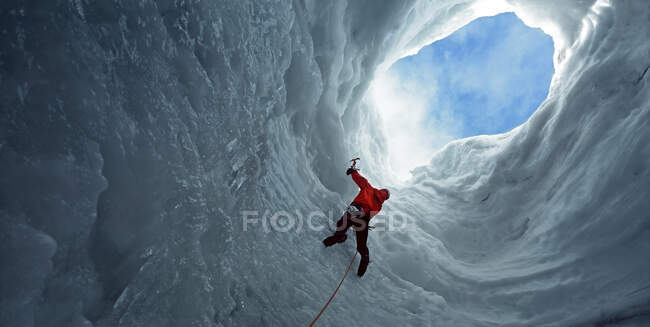 Hombre subiendo hacia una abertura en una cueva de hielo en el glaciar Langjokull - foto de stock