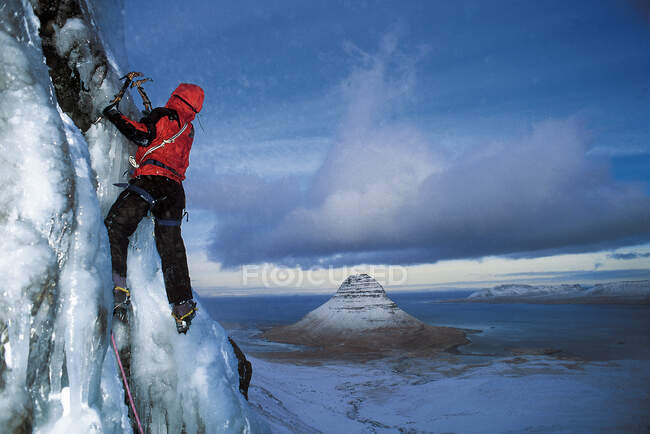 Hombre sube cascada congelada por encima del fiordo de Grundafjordur en Islandia - foto de stock