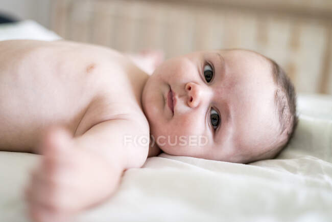 Retrato de lindo bebé sin camisa acostado en la cama en casa - foto de stock