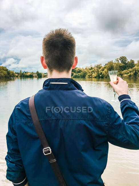 Giovane ragazzo sulla schiena con un bicchiere di champagne in mano a bordo — Foto stock