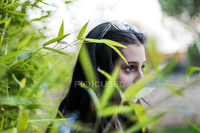 Jeune fille latéralement regardant droit devant entouré de feuilles de bambou — Photo de stock