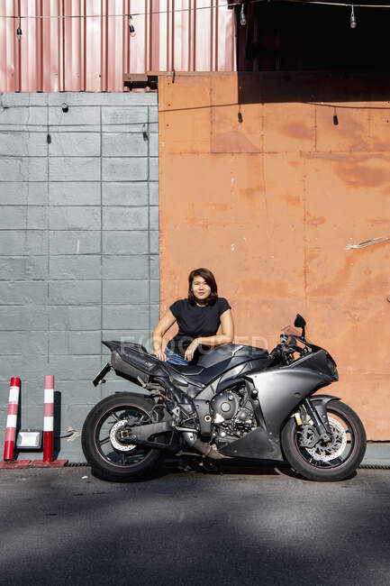 Woman leaning on her motorcycle in front of warehouse in Bangkok — Stock Photo