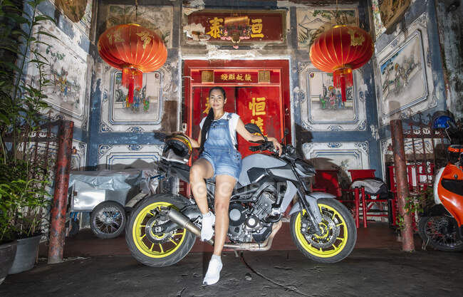 Mujer apoyada en su motocicleta frente a la casa china en Bangkok - foto de stock