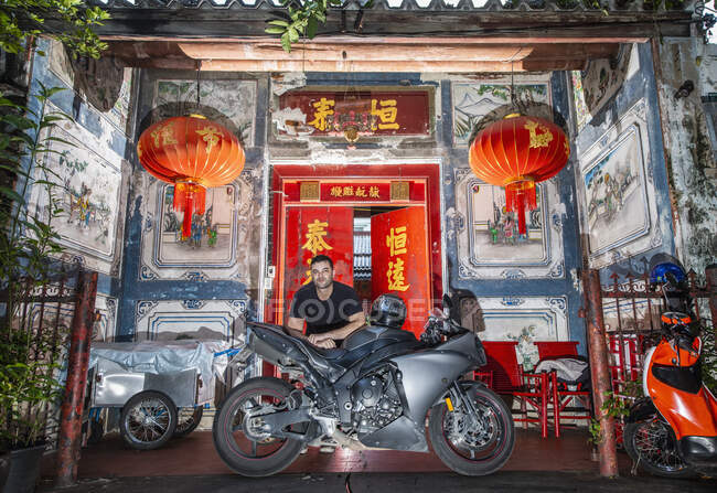 Hombre apoyado en su motocicleta frente a la casa china en Bangkok - foto de stock