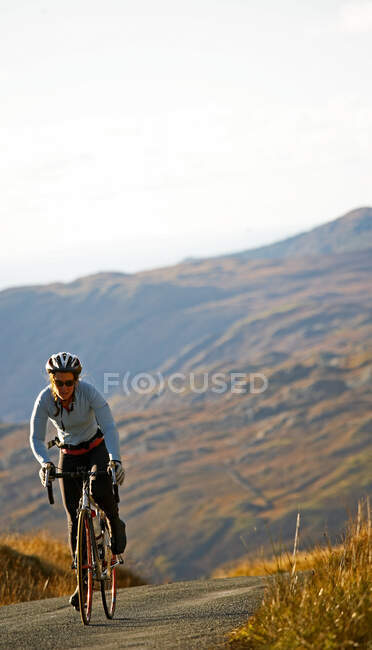 Female cyclist approaching top of a hill at the British Lake district — Stock Photo