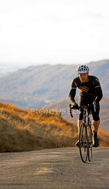 Cyclist approaching top of hill in the British Lake District — Stock Photo