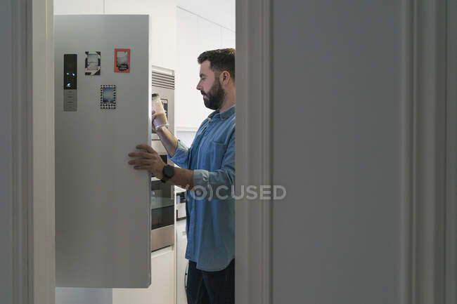 Чоловік готує на кухні, виймаючи горщик з холодильника в джинсовій сорочці — стокове фото