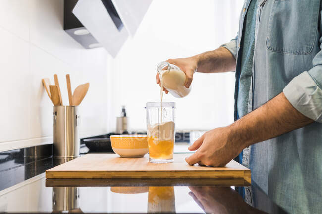 Homem de camisa jeans a cozinhar na cozinha. Homem derramando leite em um recipiente — Fotografia de Stock