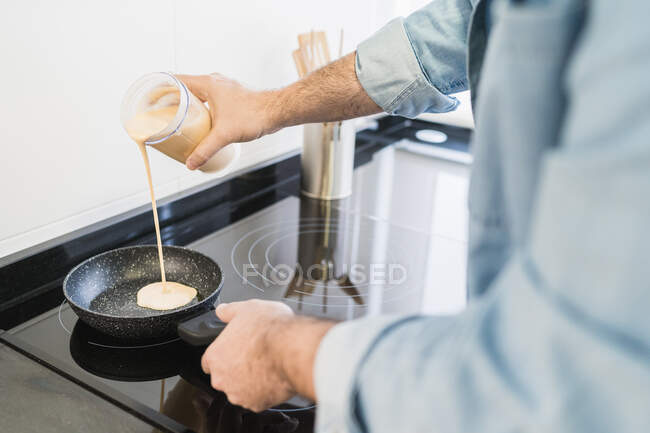 Um homem a cozinhar na cozinha. Homem derramando uma mistura de crepe na panela — Fotografia de Stock