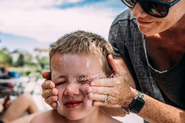 Close up of mother rubbing lotion on son's face on summer day — Stock Photo