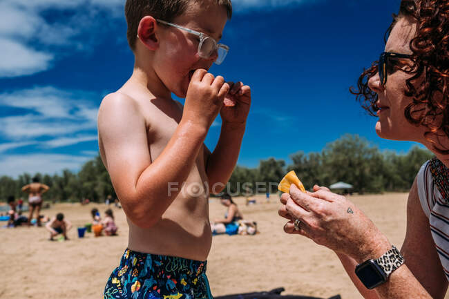 Primer plano de madre dando hijo un bocadillo en la playa - foto de stock