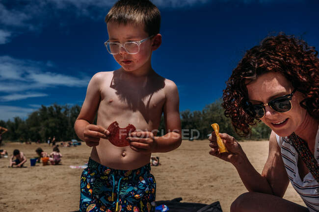 Мальчик ест мясо и сыр на пляже — стоковое фото