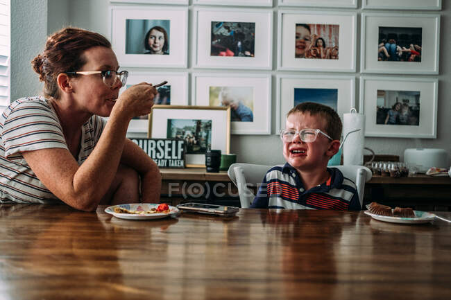 Junge mit Wutanfällen, während Mama in der Nähe Kuchen isst — Stockfoto