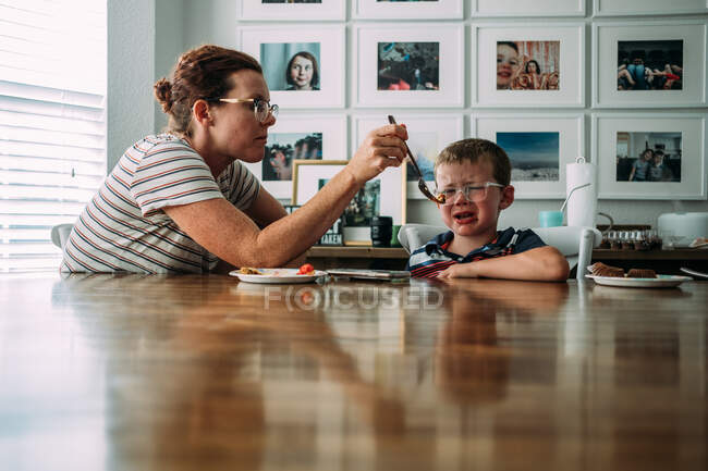 Мама кормит маленького сына кусочком торта за столом — стоковое фото