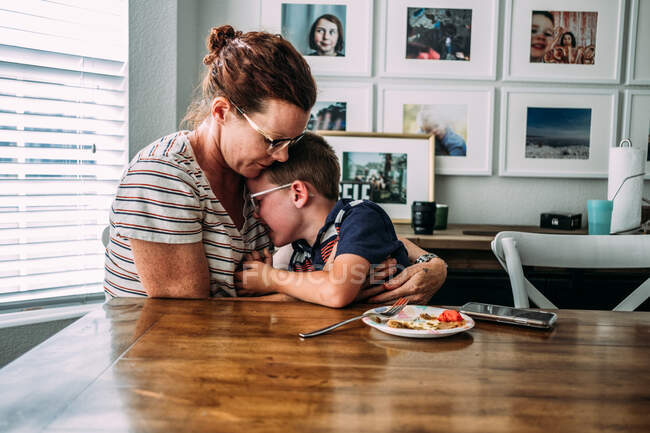 Mom hugging sad young boy at dinner table — Stock Photo