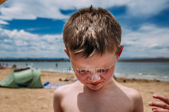 Gros plan de jeune garçon à la plage avec écran solaire sur le nez — Photo de stock