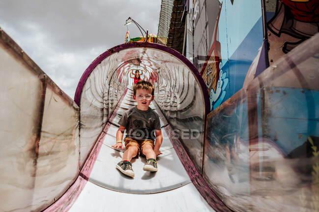 Porträt eines gelangweilten Jungen, der auf dem Jahrmarkt eine große Rutsche hinunterrutscht — Stockfoto