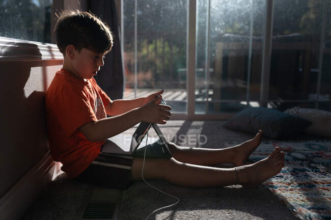 Хлопчик використовує планшет ipad на підлозі свого будинку з сонцем у вікні — стокове фото