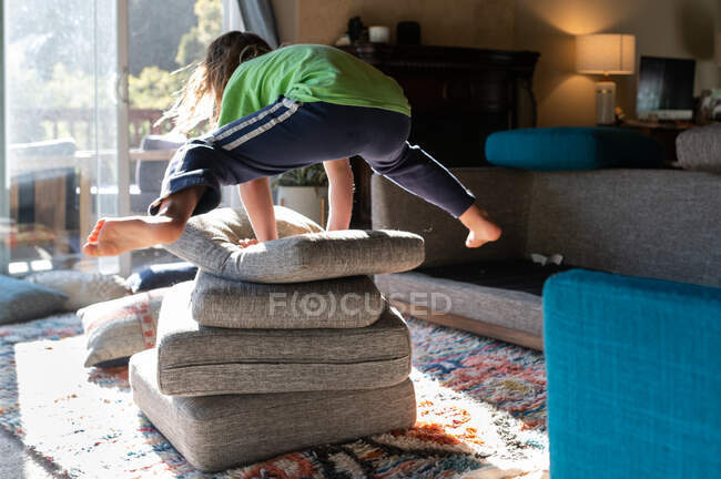 Kind springt im Wohnzimmer über einen Stapel Couchkissen — Stockfoto