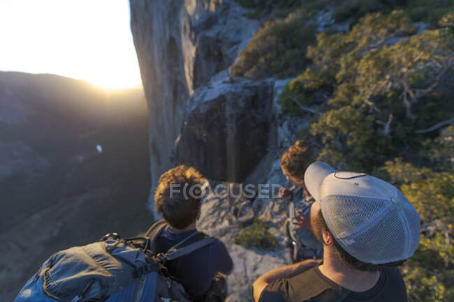 Three hikers looking at The Nose El Capitan from the top at sunset — Stock Photo