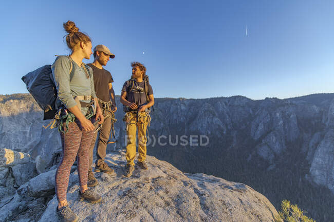 Tres excursionistas en la cima de El Capitán en el Valle de Yosemite al atardecer - foto de stock