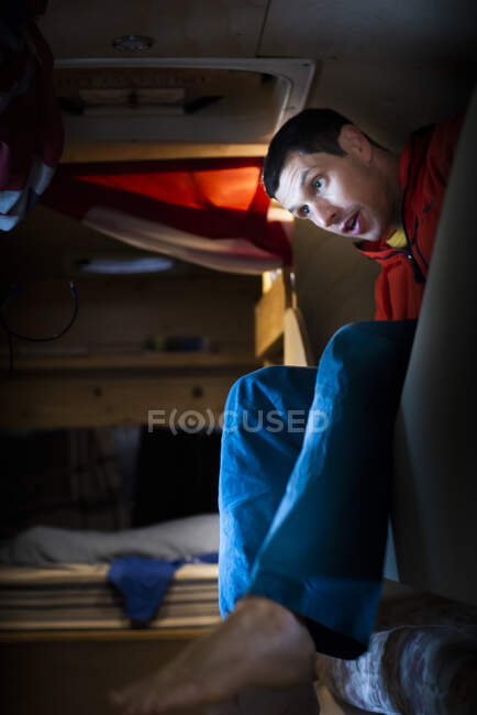 Чоловік прокидається з двоярусного ліжка всередині перетвореного шкільного автобуса, одягненого — стокове фото