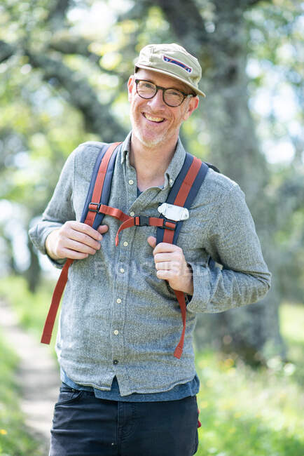 Portrait of smiling hiker with hat, glasses, and backpack outdoors — Stock Photo