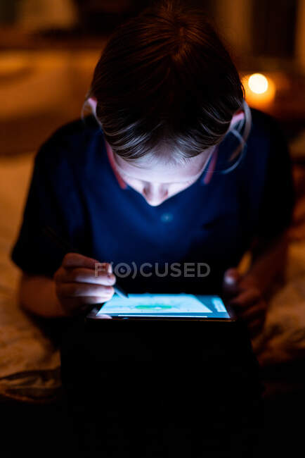 Teenager zeichnet auf Tablet mit hellem Bildschirm und Stift bei wenig Licht — Stockfoto