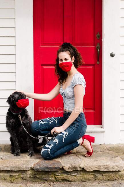 Joven mujer con estilo y perro con máscara durante la pandemia COVID19 - foto de stock