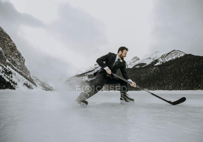 Young man in a suit playing hockey in winter frozen ice — Stock Photo