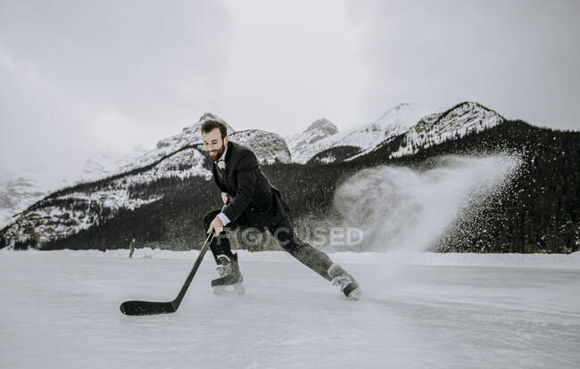 Молодой человек в костюме играет в хоккей зимой замороженный лед — стоковое фото