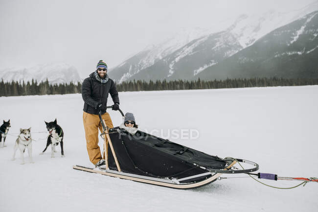 Mann und Frau sitzen und stehen in Hundeschlitten in kanadischen Rockies — Stockfoto