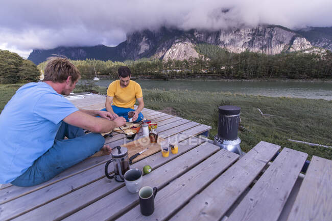 Пара сидит на скамейке и пьет кофе на озере — стоковое фото