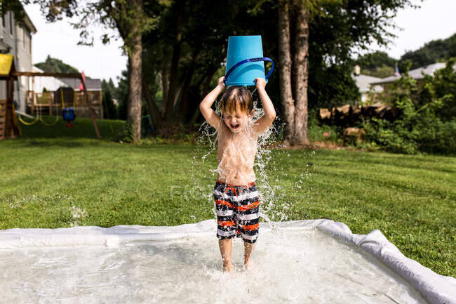 Niño joven vertiendo cubo de agua sobre la cabeza - foto de stock