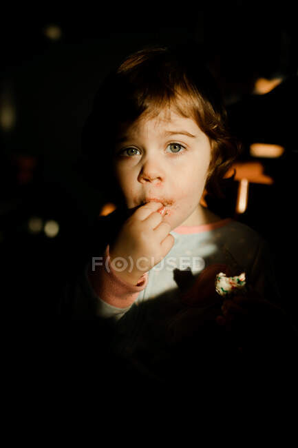 Bambino che mangia biscotti di zucchero in pigiama su una sedia in cucina — Foto stock