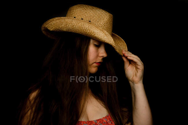 Triste dama en sombrero de vaquero inclinando su sombrero hacia abajo en luz dramática - foto de stock