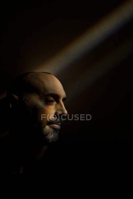 Mann sitzt im Regenbogenstrahl an dunkler Wand im Keller — Stockfoto
