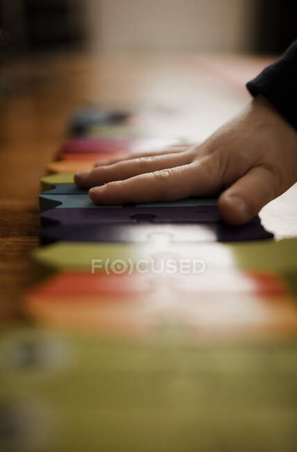 Mano de niño preescolar armando un rompecabezas de colores brillantes - foto de stock