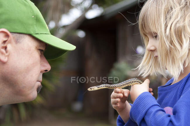 Батько і дочка тримають гофровану змію в саду — стокове фото