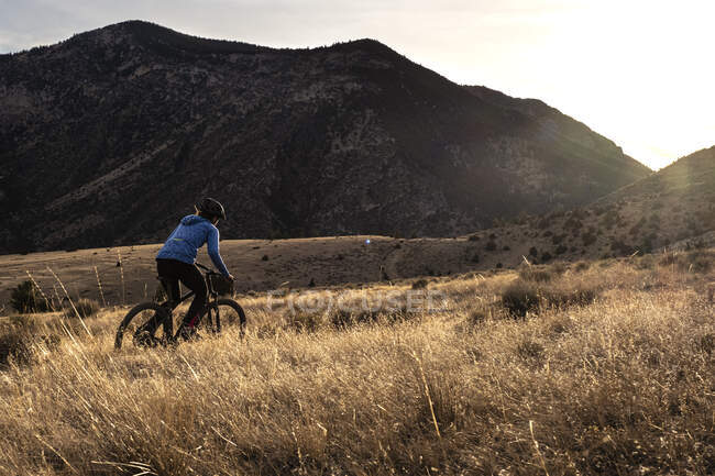 Young woman mountain biking uphill during sunset in mountains — Stock Photo