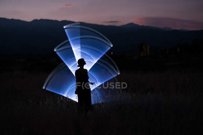 Silhueta de mulher através de luz azul lightpainting ao pôr do sol no — Fotografia de Stock