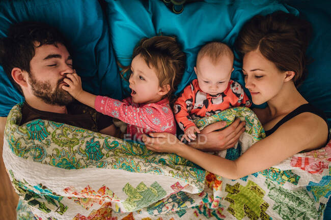 Family of four crowded in bed needing personal space and pushing away — Stock Photo