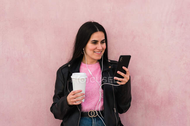 Jeune femme écouter de la musique et regarde son smartphone dans un dos rose — Photo de stock